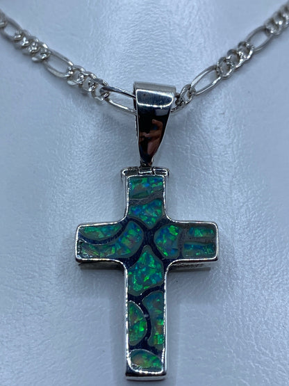 Cruz de plata con ópalo que refleja tonos verdes y azules, vista lateral