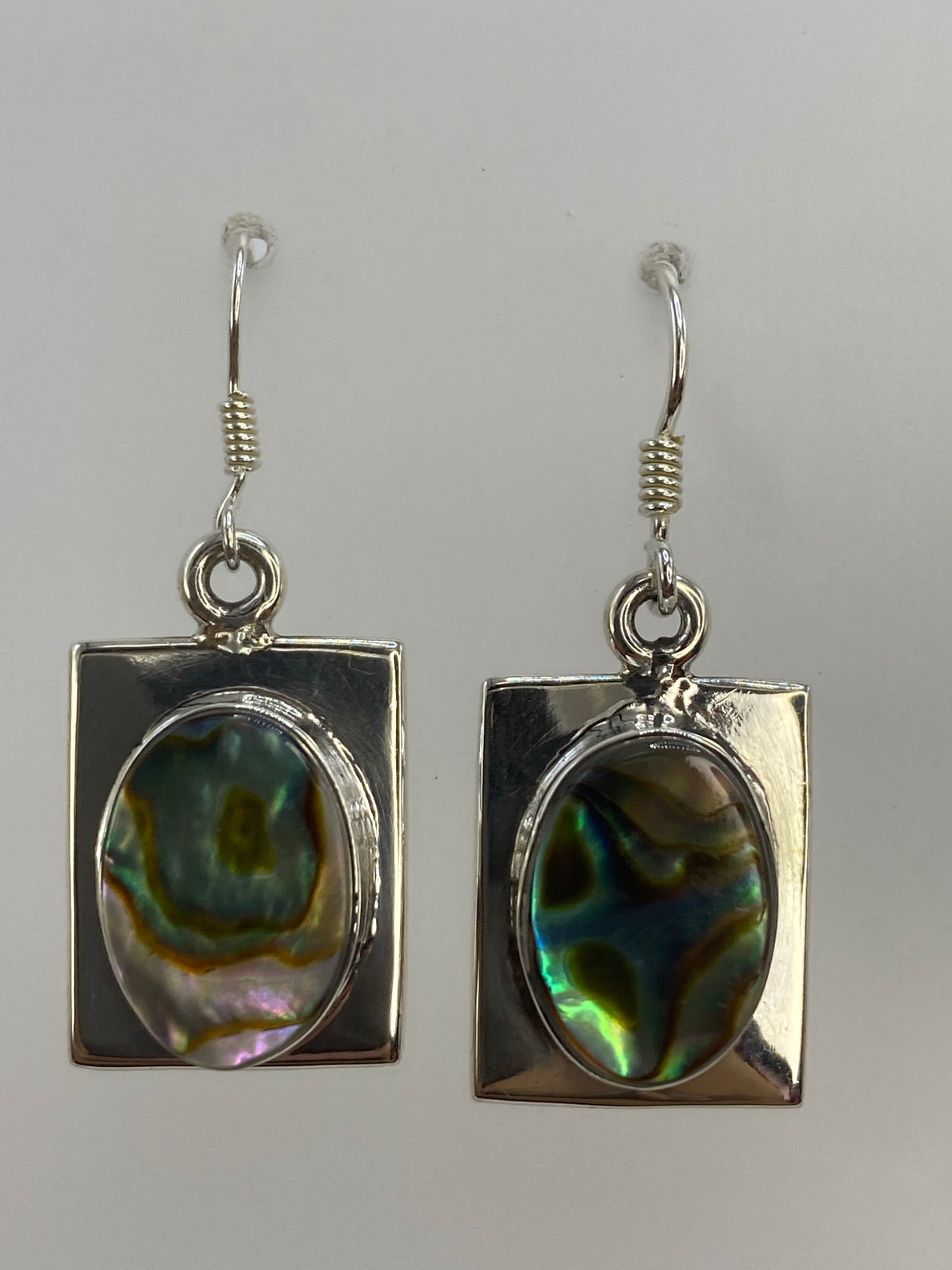 Par de aretes de plata con concha de abulón iridiscente, reflejos azul y verde en fondo gris