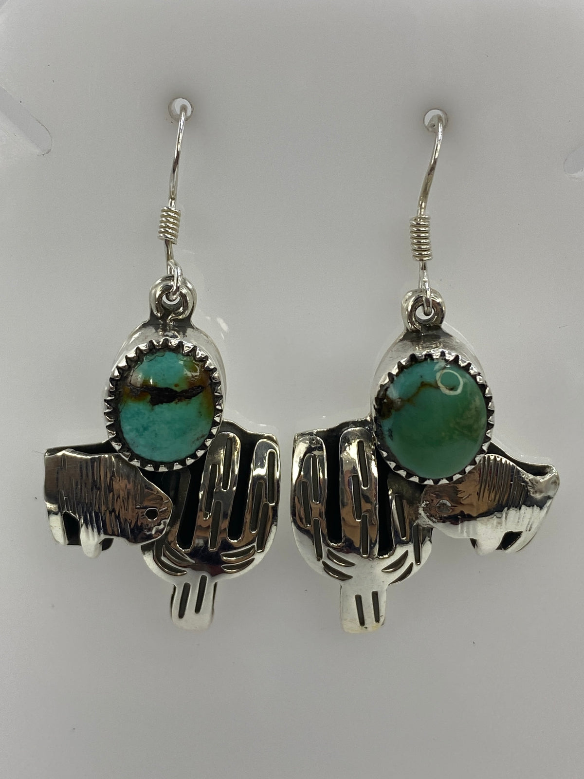 Par de aretes de plata con motivo de cactus y turquesa azul, colgando sobre fondo blanco