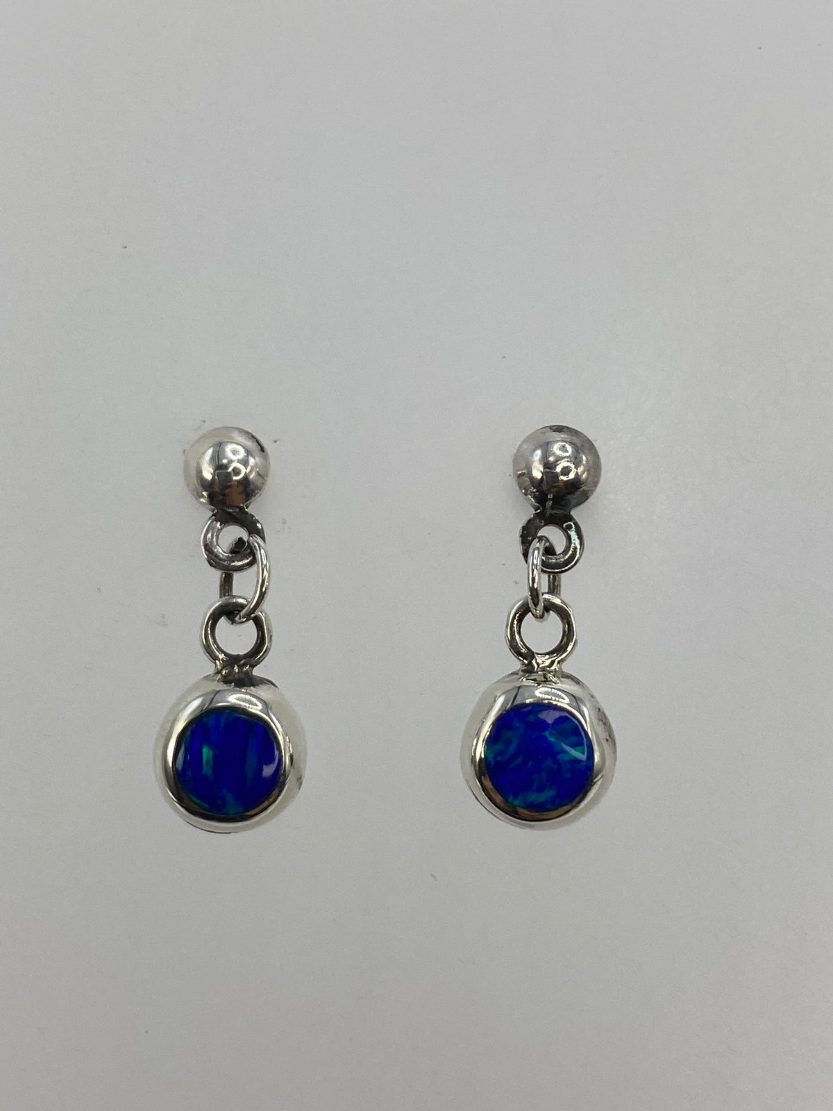Par de aretes de plata con ópalo de fuego azul engastado, vistos de frente