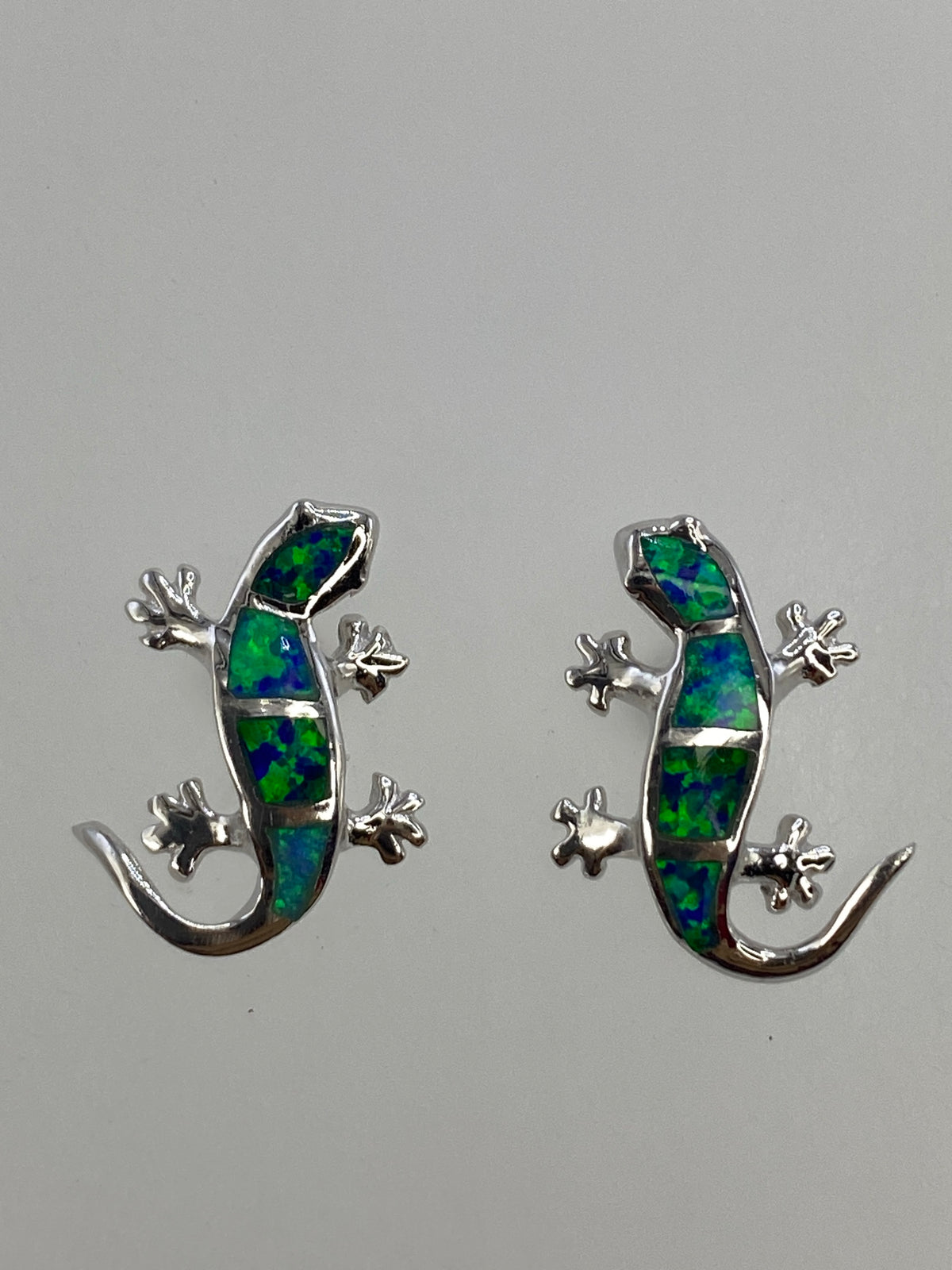 Aretes de lagartija sobre regla mostrando tamaño exacto de 1.7 × 1.4 cm