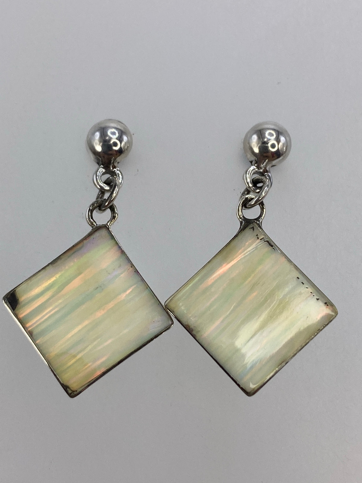 Par de aretes de plata cuadrados con madre perla blanca incrustada, vistos de frente sobre fondo neutro