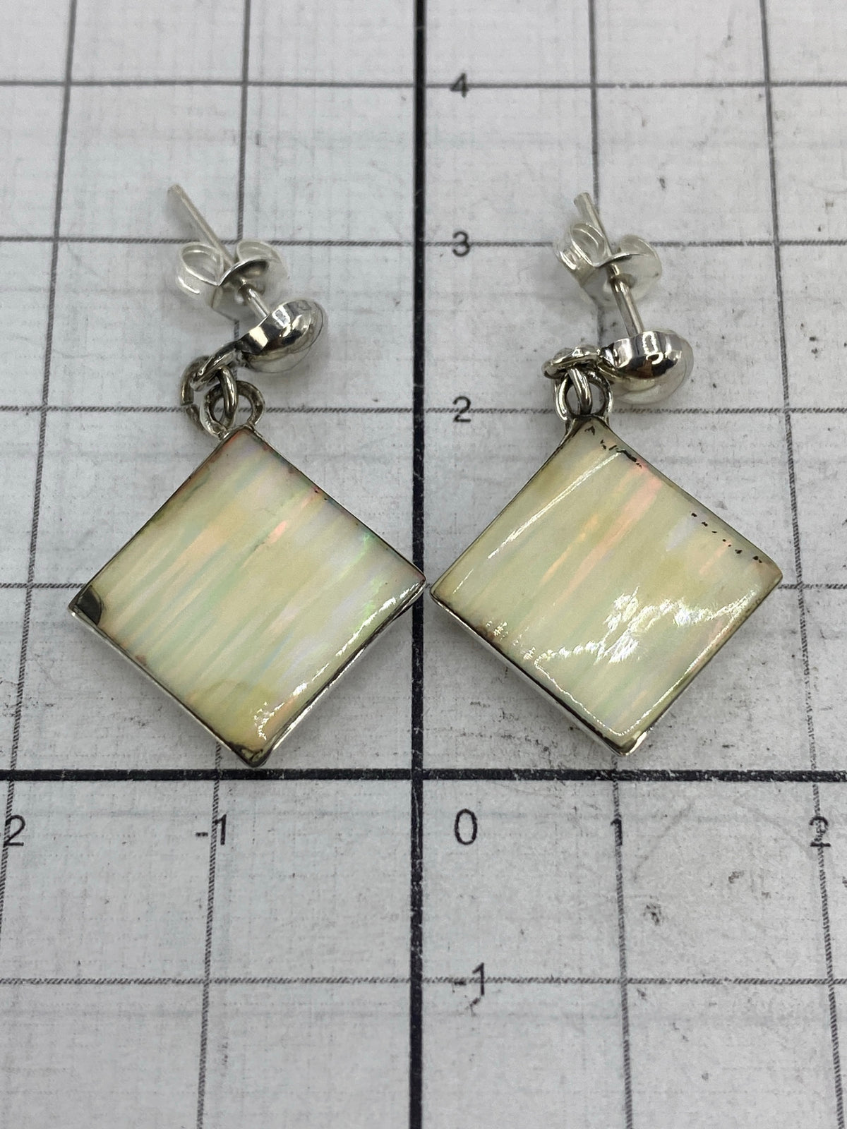 Aretes sobre regla de centímetros confirmando las medidas 3 cm × 1.7 cm por pieza