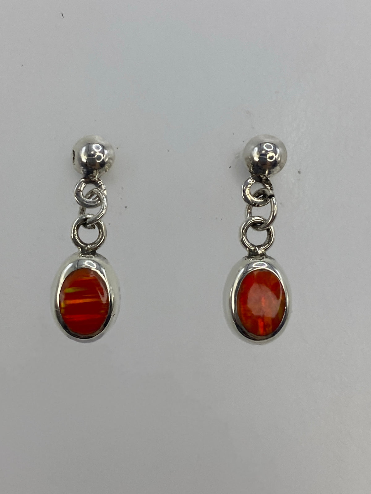 Pair of sterling silver earrings with vibrant orange fire opal drops, shown from front
