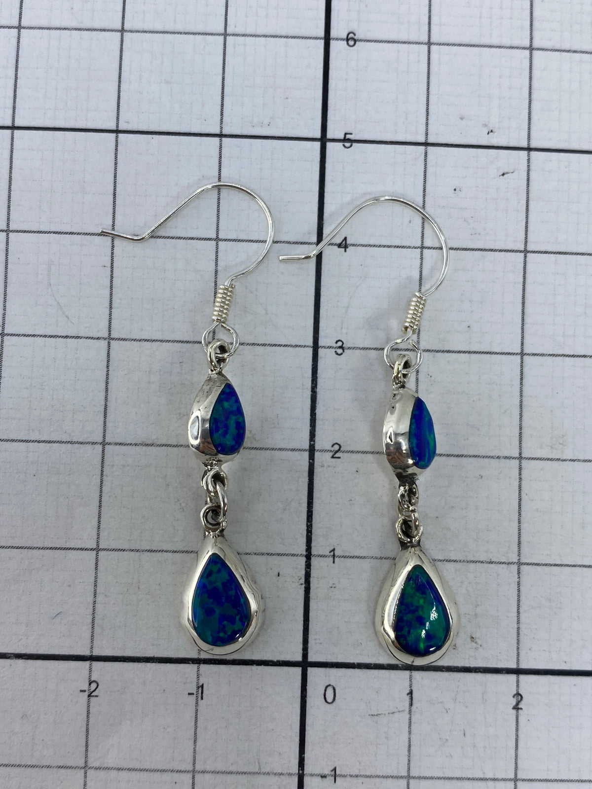Aretes de plata sobre fondo azul, mostrando destellos verdes del ópalo de fuego