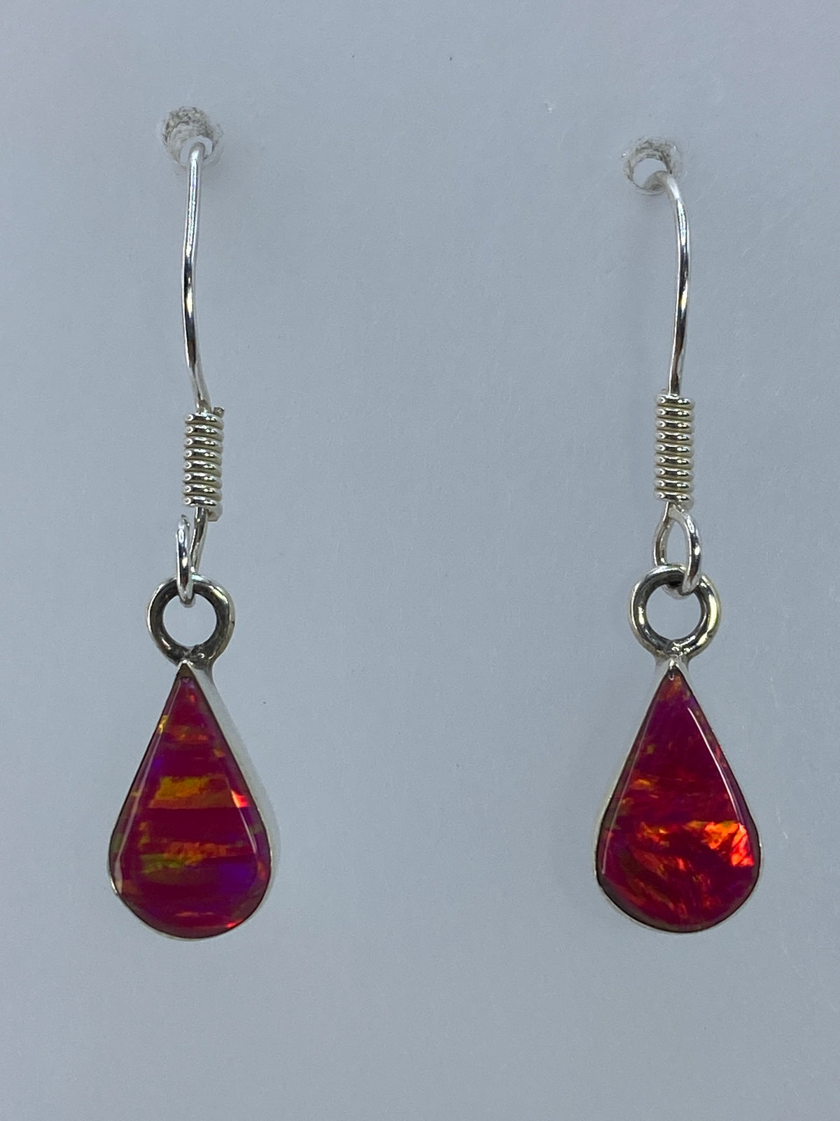 Par de aretes de plata con ópalo de fuego rosa colgando sobre fondo gris