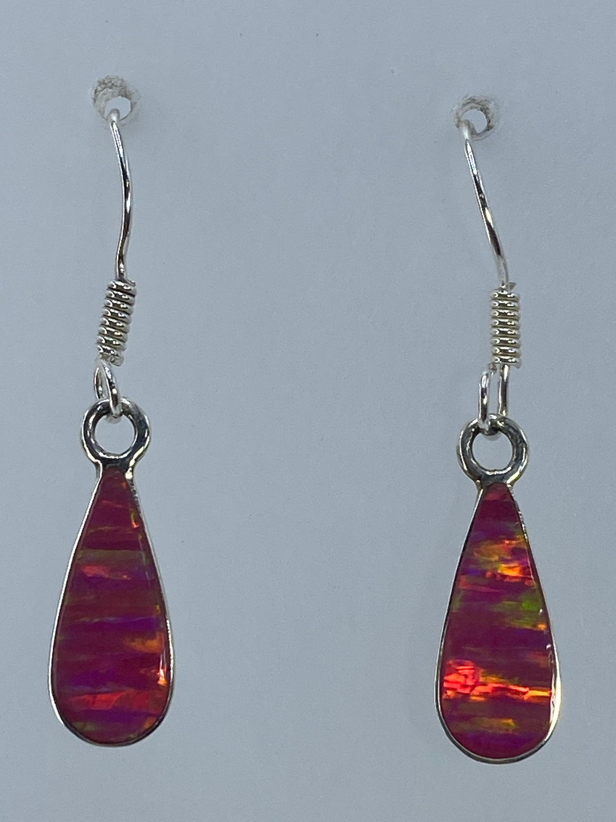 Aretes de plata con ópalo de fuego rosa en tono romántico, colgando sobre fondo gris