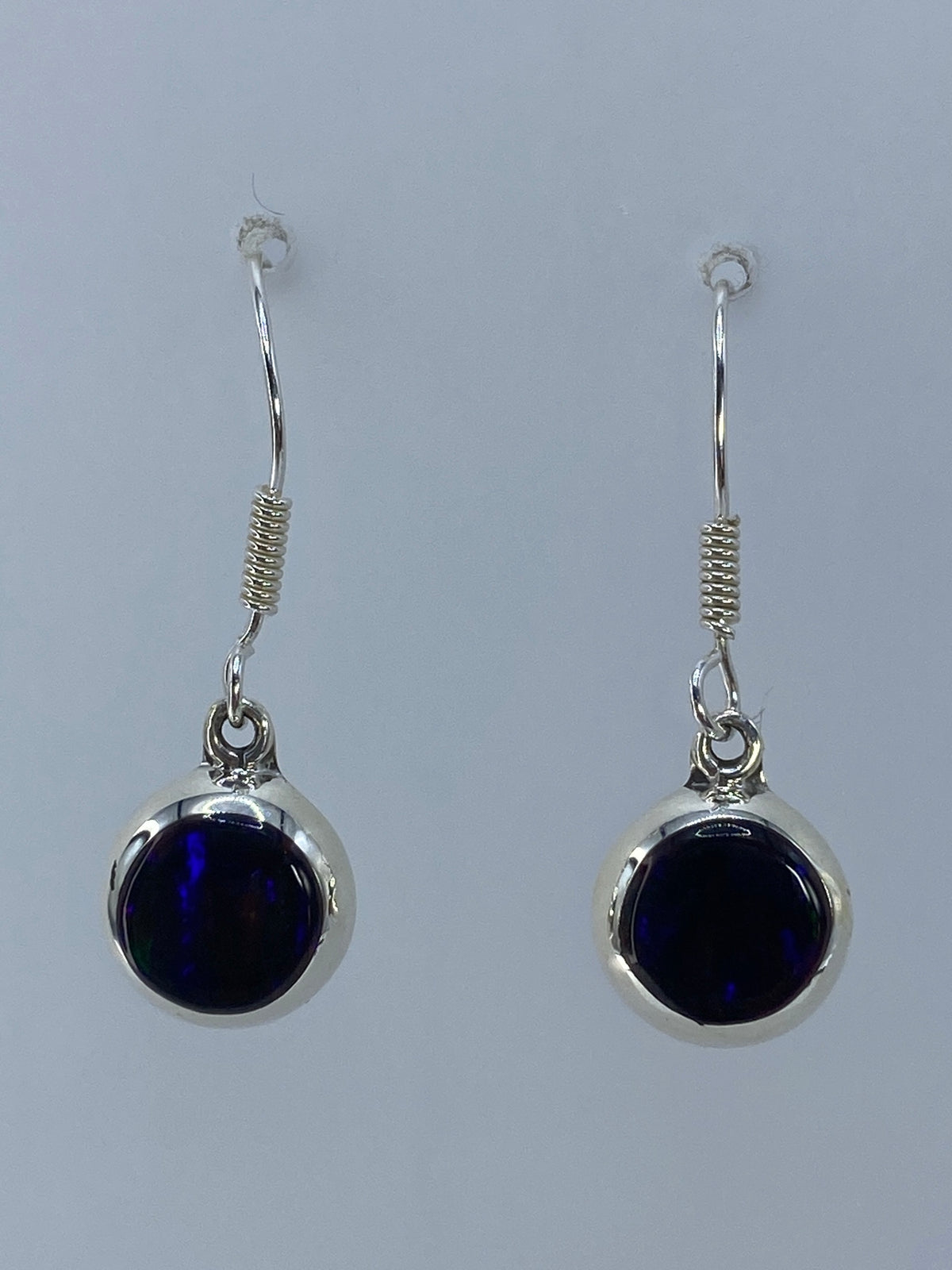 Par de aretes de plata con ópalo de fuego morada engastado, colgando sobre fondo blanco