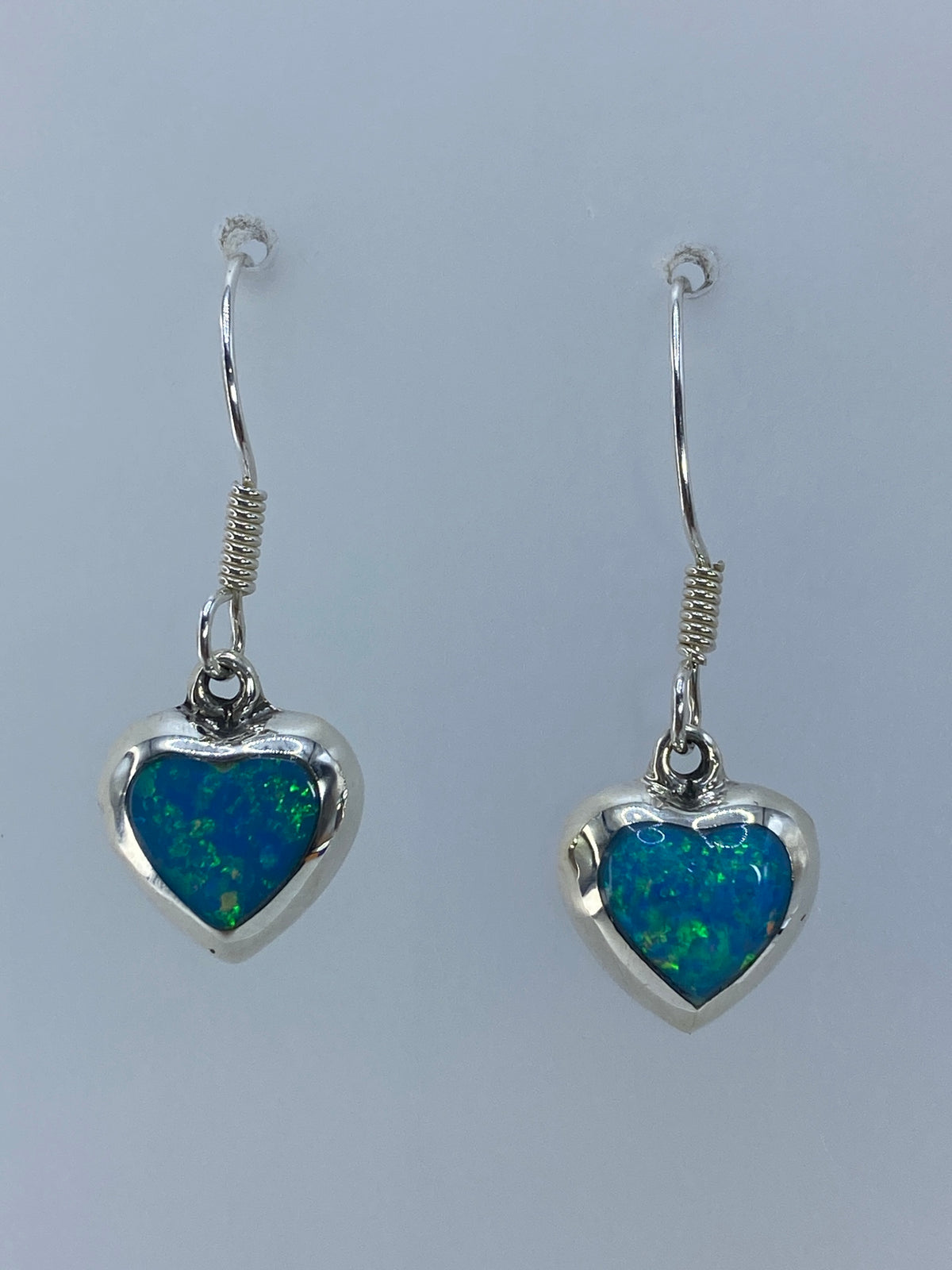 Aretes colgando mostrando el color verde olivo y reflejos del ópalo de fuego