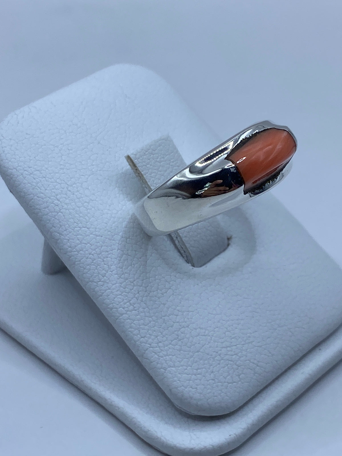 Anillo de coral y plata usado en la mano, mostrando el brillo del engaste