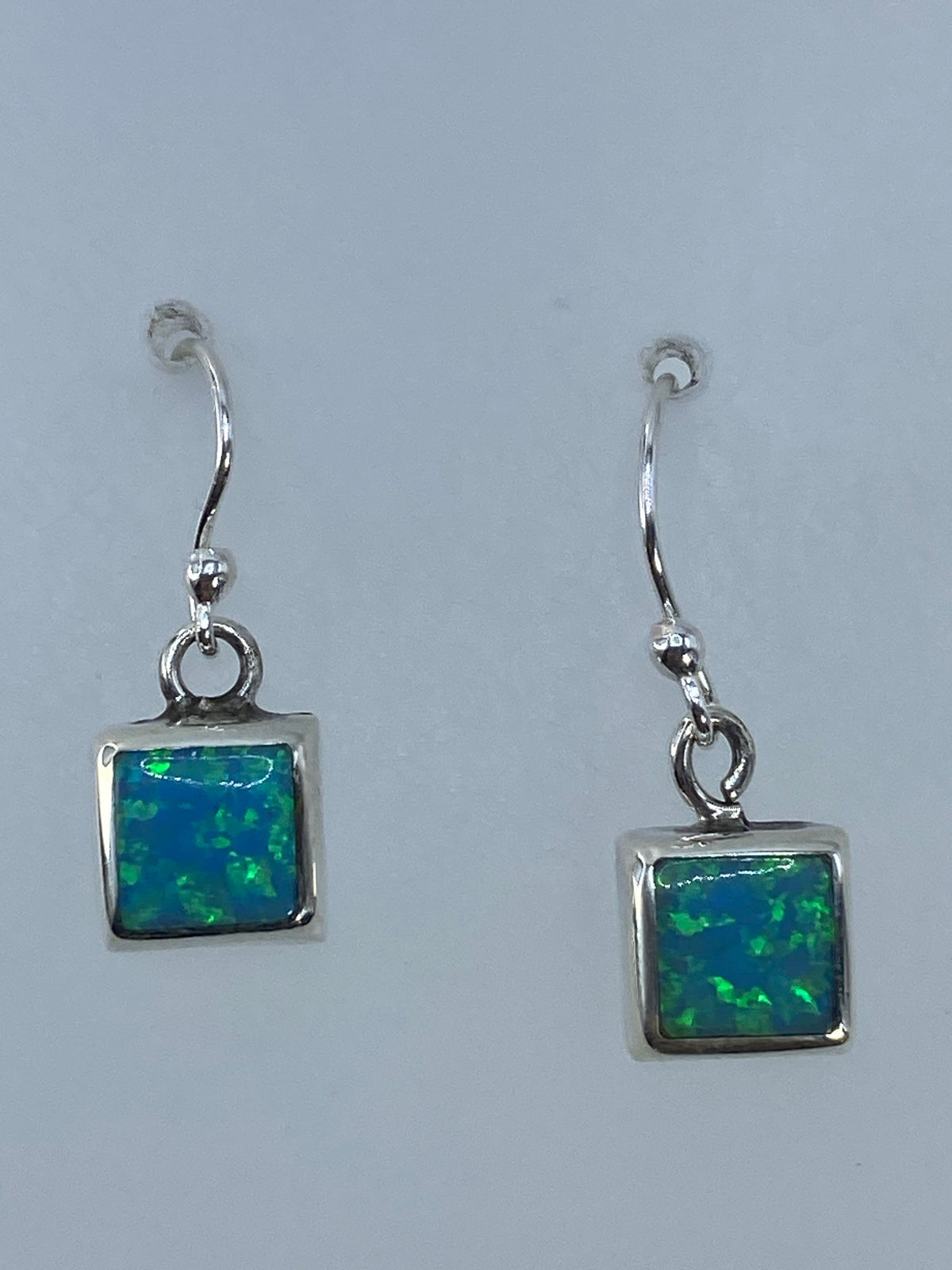 Aretes en la mano mostrando el color verde olivo del ópalo con luz natural
