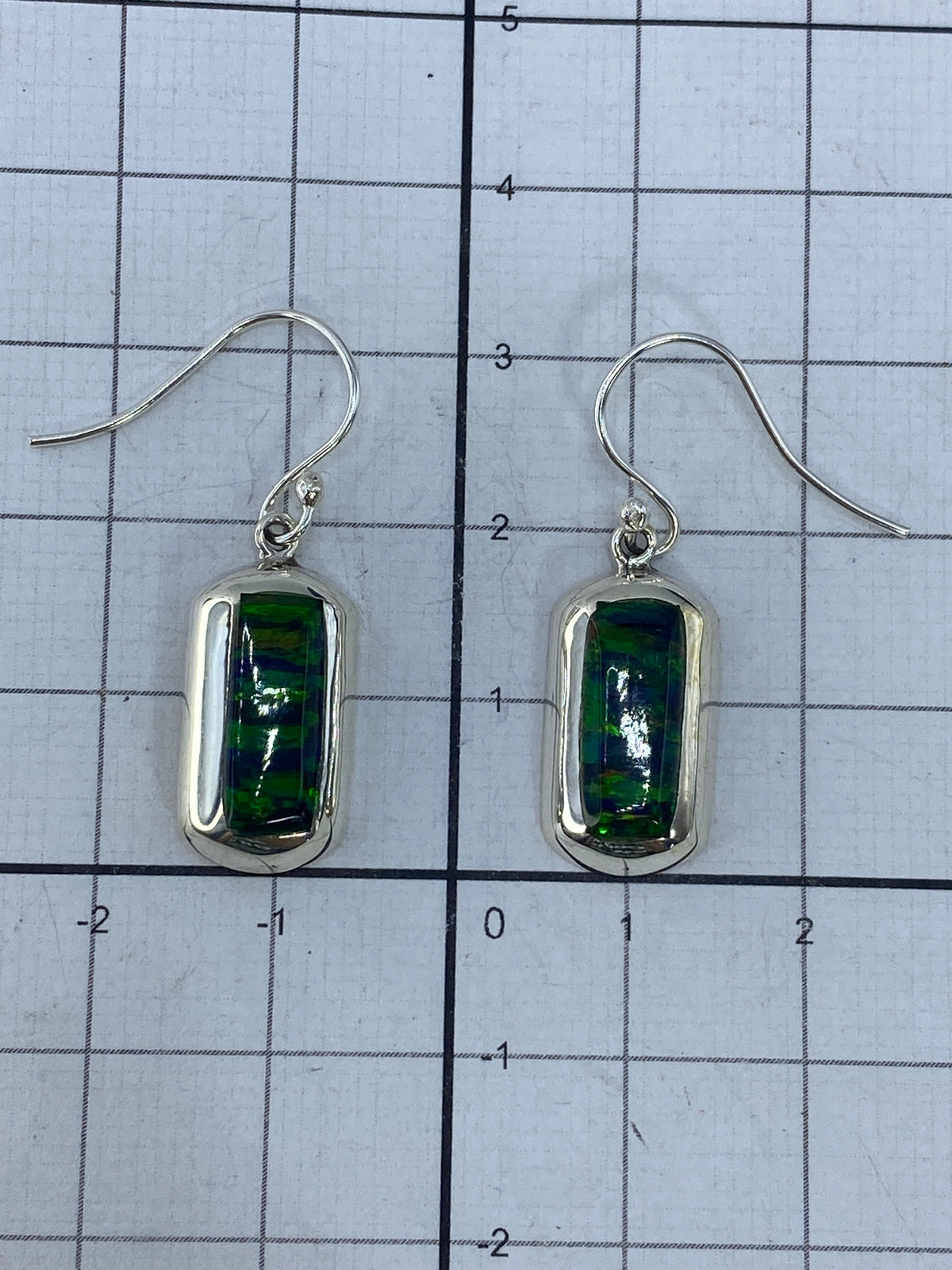 Aretes de plata colgando, mostrando el engaste a mano del ópalo y la refracción de luz verde
