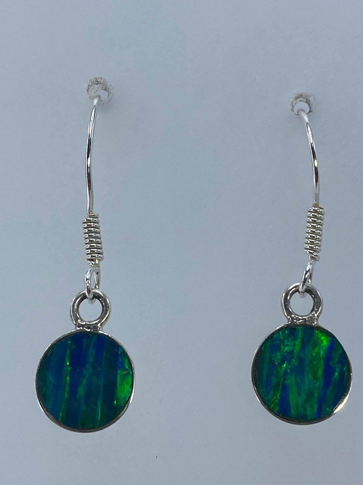 Aretes de ópalo colgando sobre fondo neutro mostrando el color verde olivo