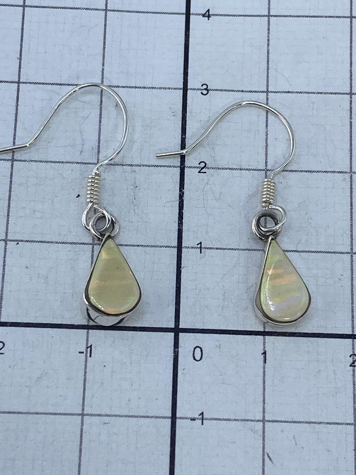 Aretes de plata con ópalo sobre fondo blanco, mostrando la pureza del metal y el Quinto