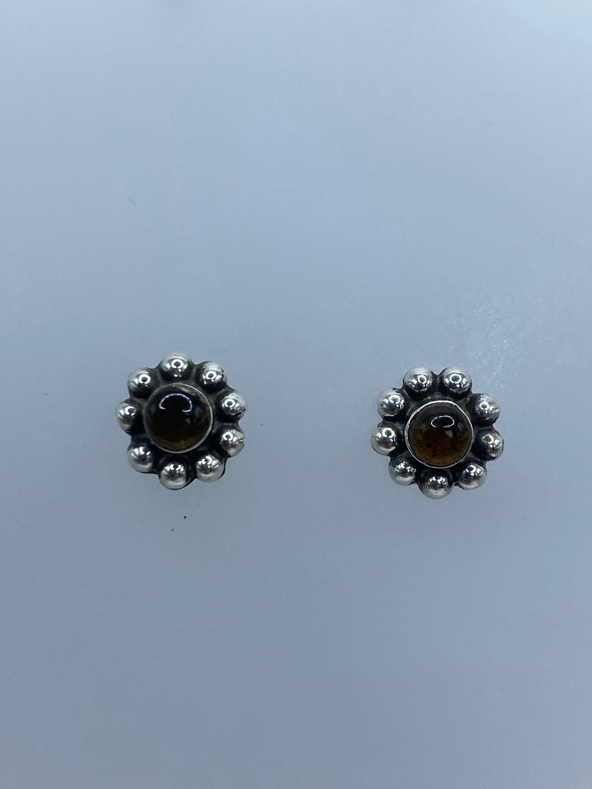 Aretes de plata con ámbar café engastado, vistos de frente sobre fondo gris
