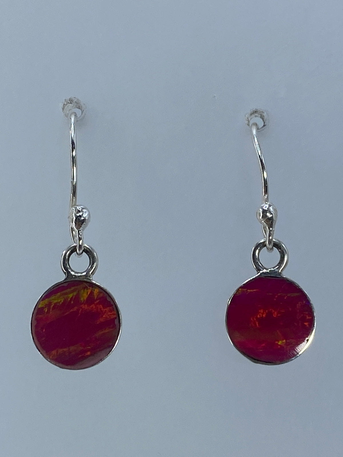 Par de aretes de plata con ópalo de fuego rosa, colgando sobre fondo gris