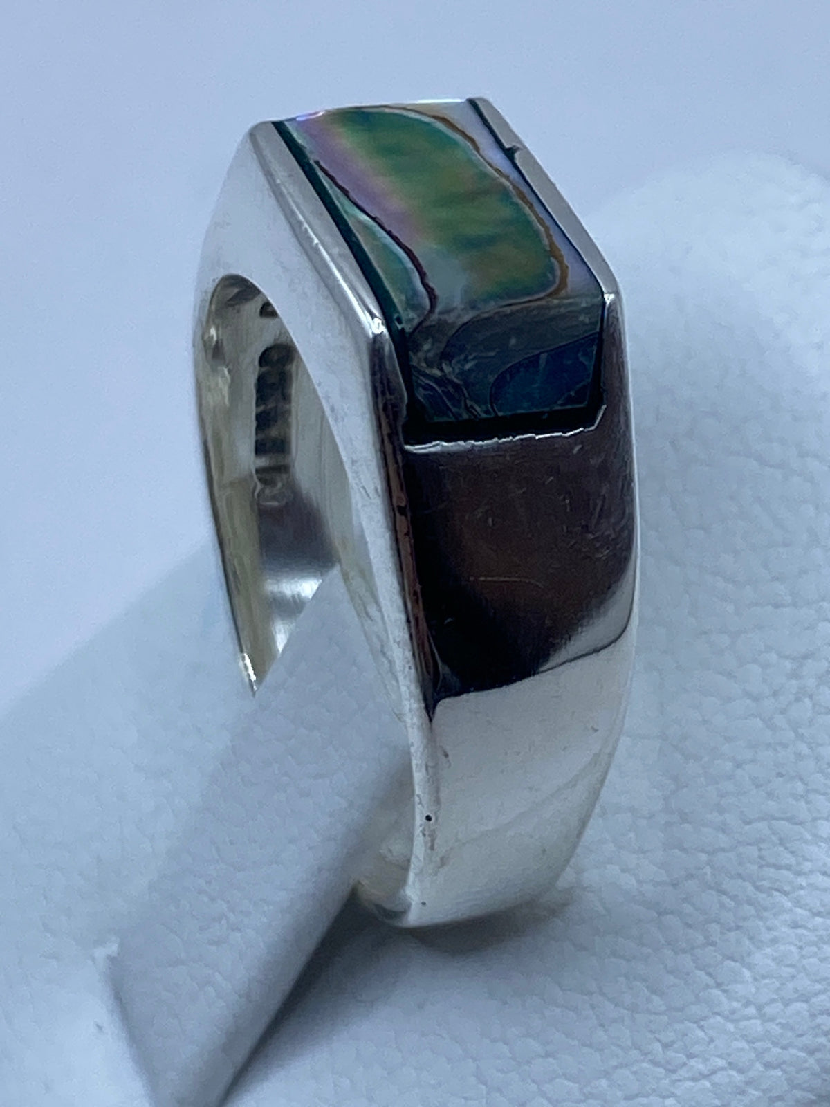 Vista lateral del anillo de plata con concha de abulón sobre fondo blanco