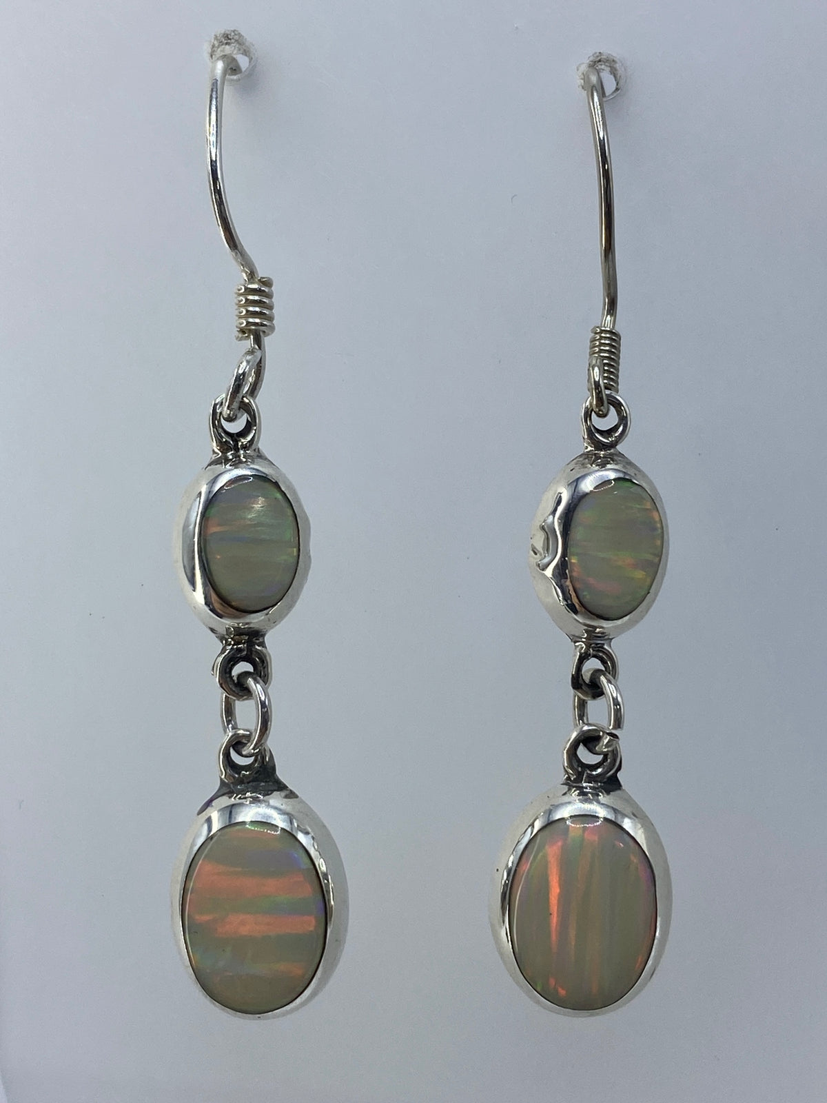 Aretes de plata con ópalo de fuego multicolor colgando, mostrando destellos rojos y naranjas
