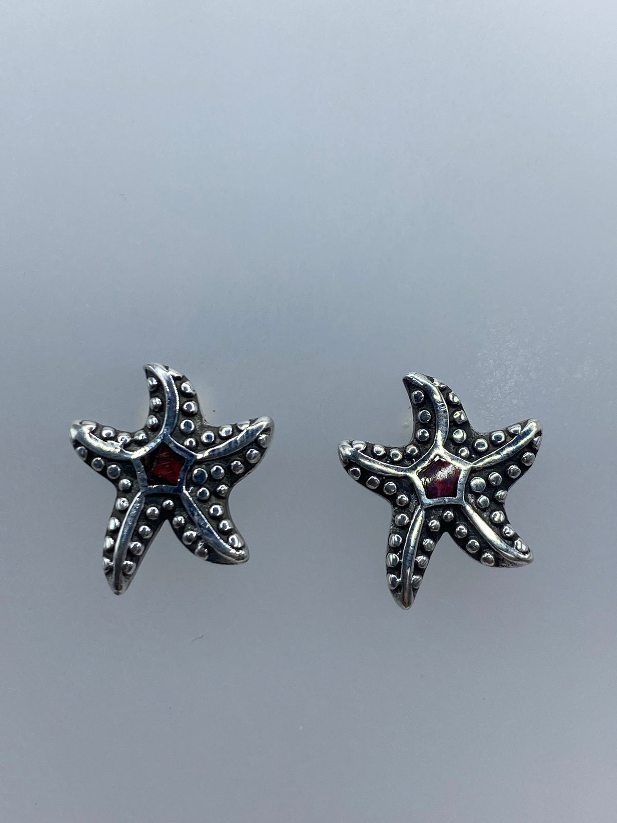 Par de aretes de plata con ópalo de fuego rojo engastado, sobre fondo gris