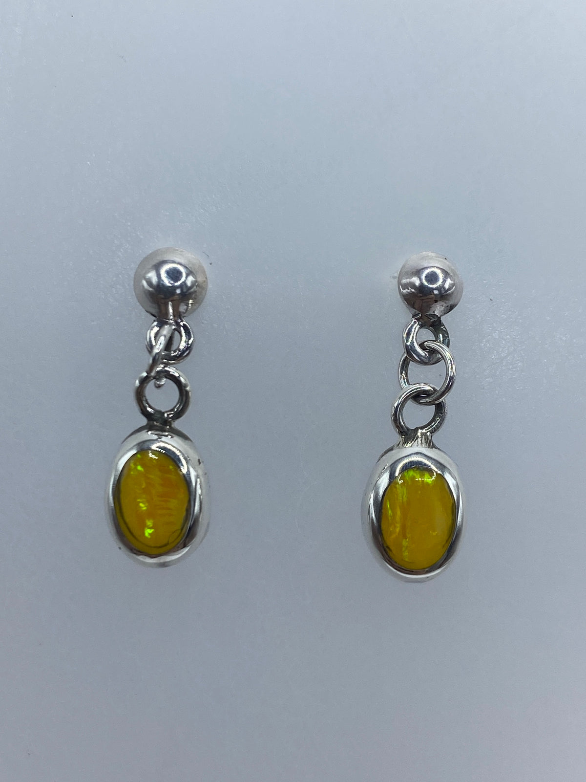 Par de aretes de plata 925 con ópalo de fuego amarillo, colgando sobre fondo gris