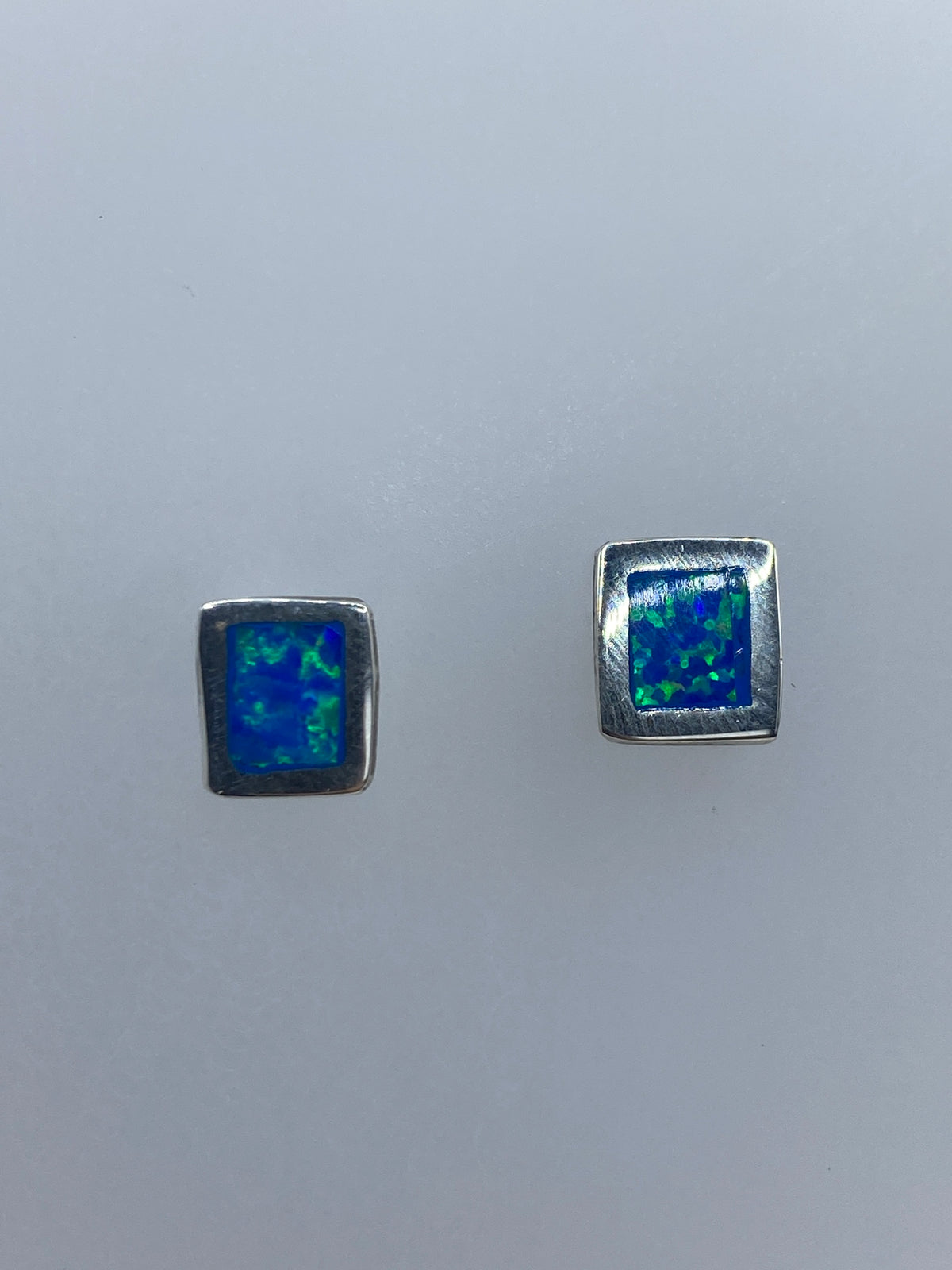 Par de aretes de plata 950 con ópalo de fuego azul engastado, sobre superficie gris