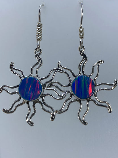 Par de aretes de plata con ópalo de fuego multicolor colgando, mostrando los destellos azul, rojo y verde de la piedra