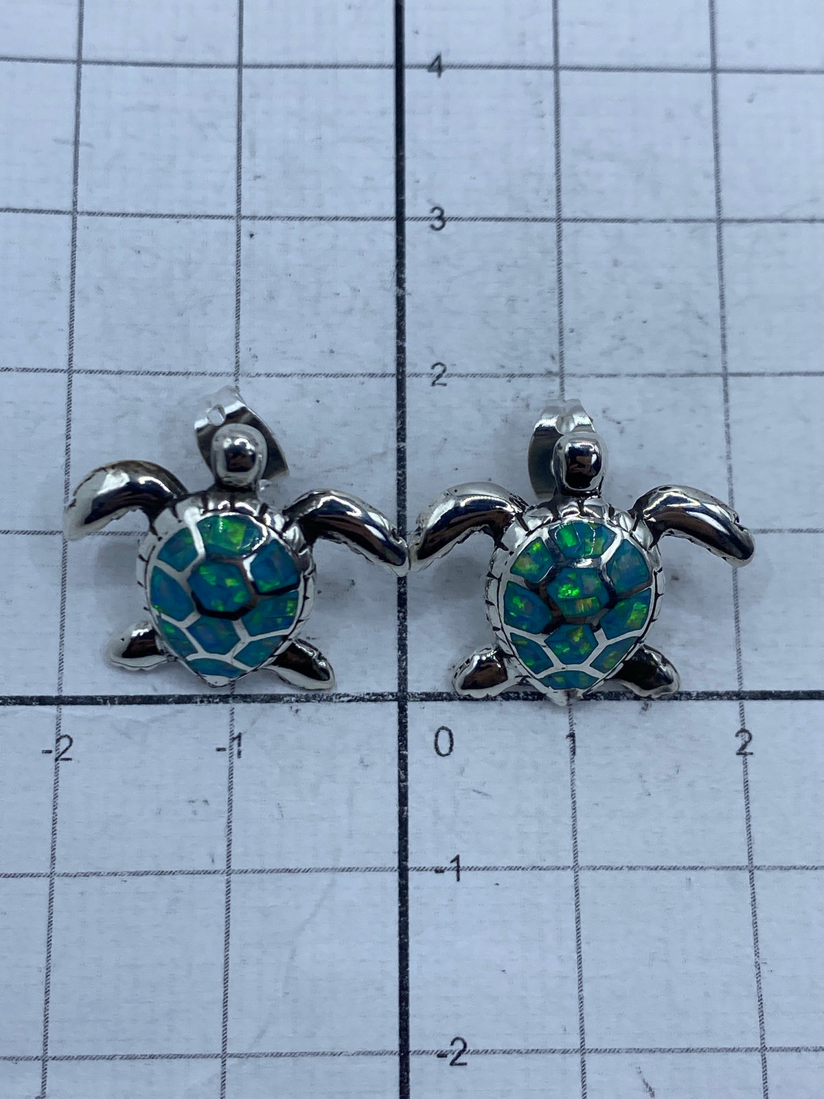 Aretes tortuga en escala, junto a regla de centímetros: 1.7 cm de largo × 2 cm de ancho