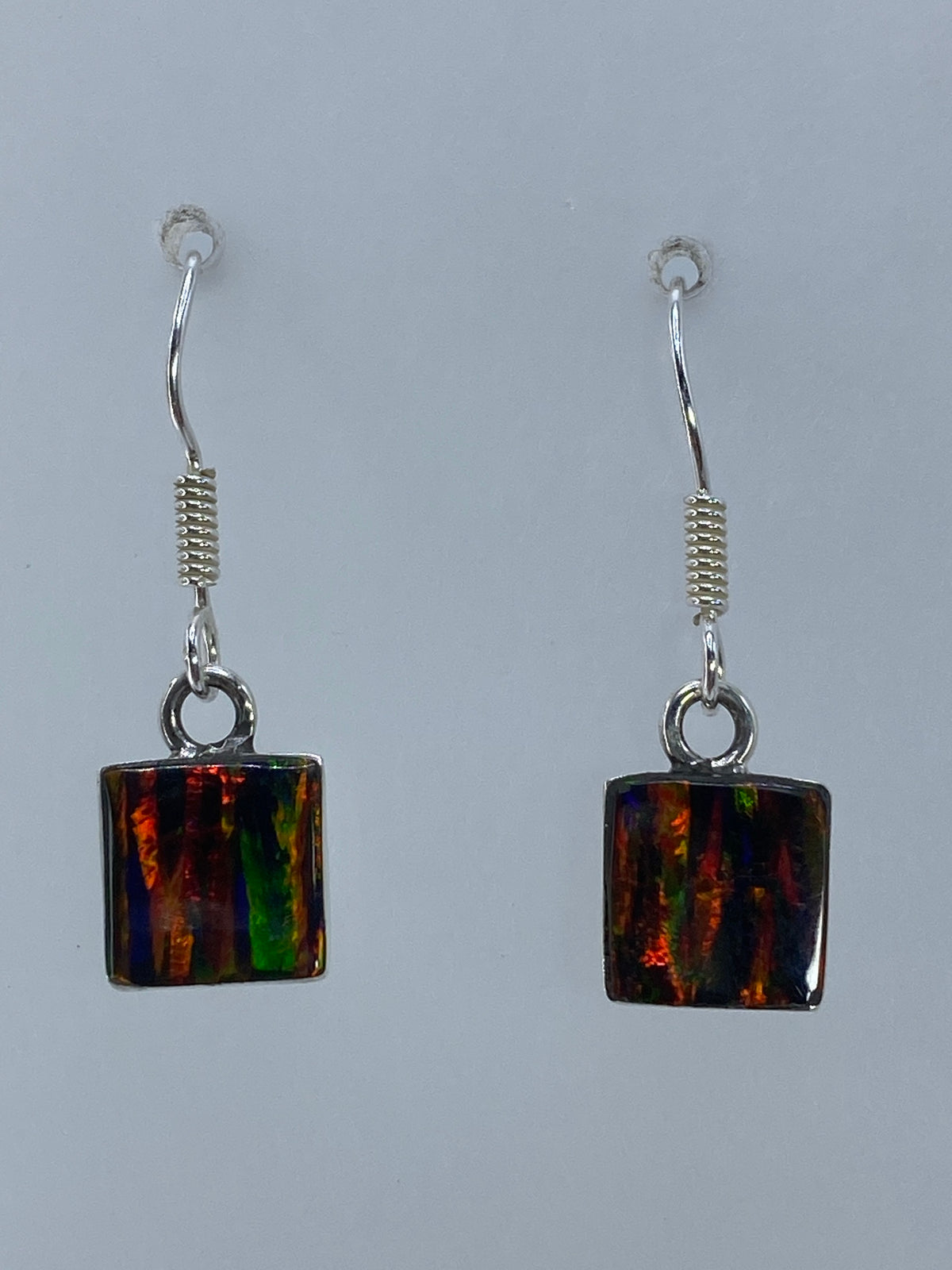 Par de aretes de plata con ópalo de fuego multicolor mostrando destellos rojos, naranjas y verdes