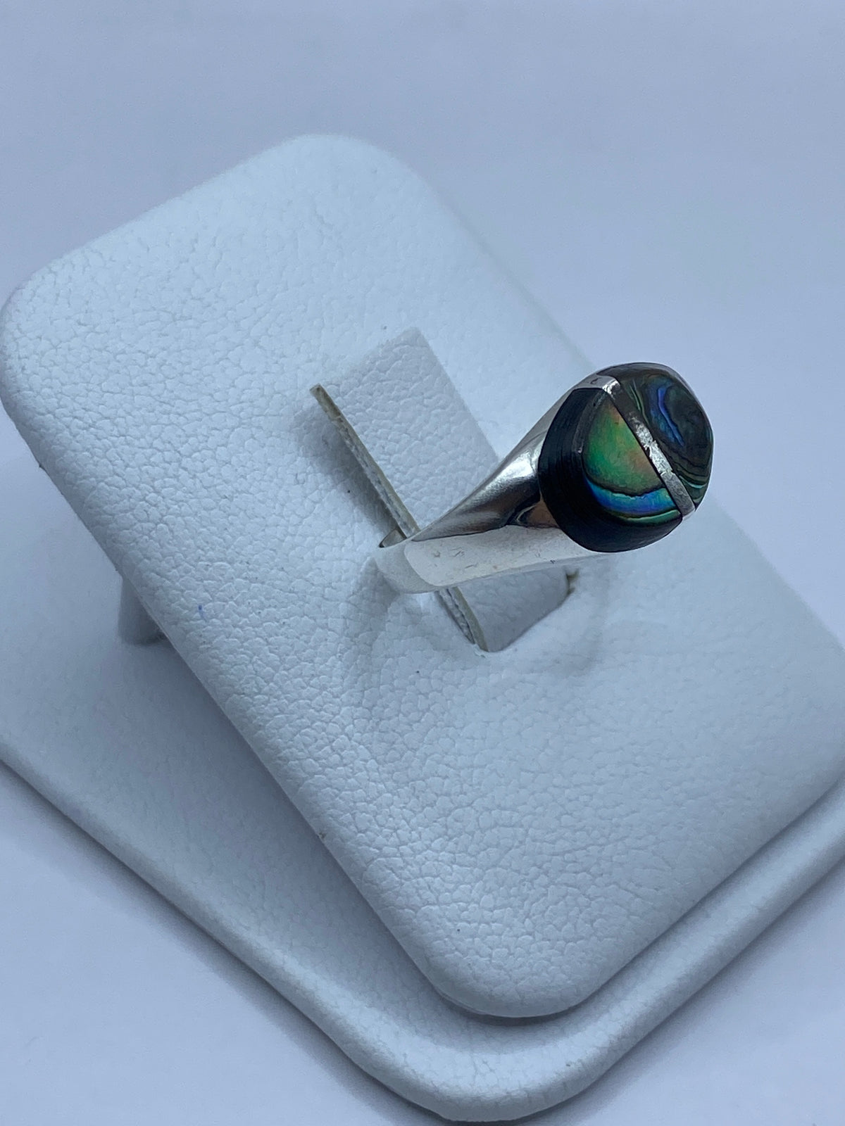 Anillo de concha de abulón en la mano, mostrando reflejos azul verdoso