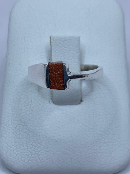 Anillo de plata solitario con piedra café rectangular engastada, vista frontal sobre dedo
