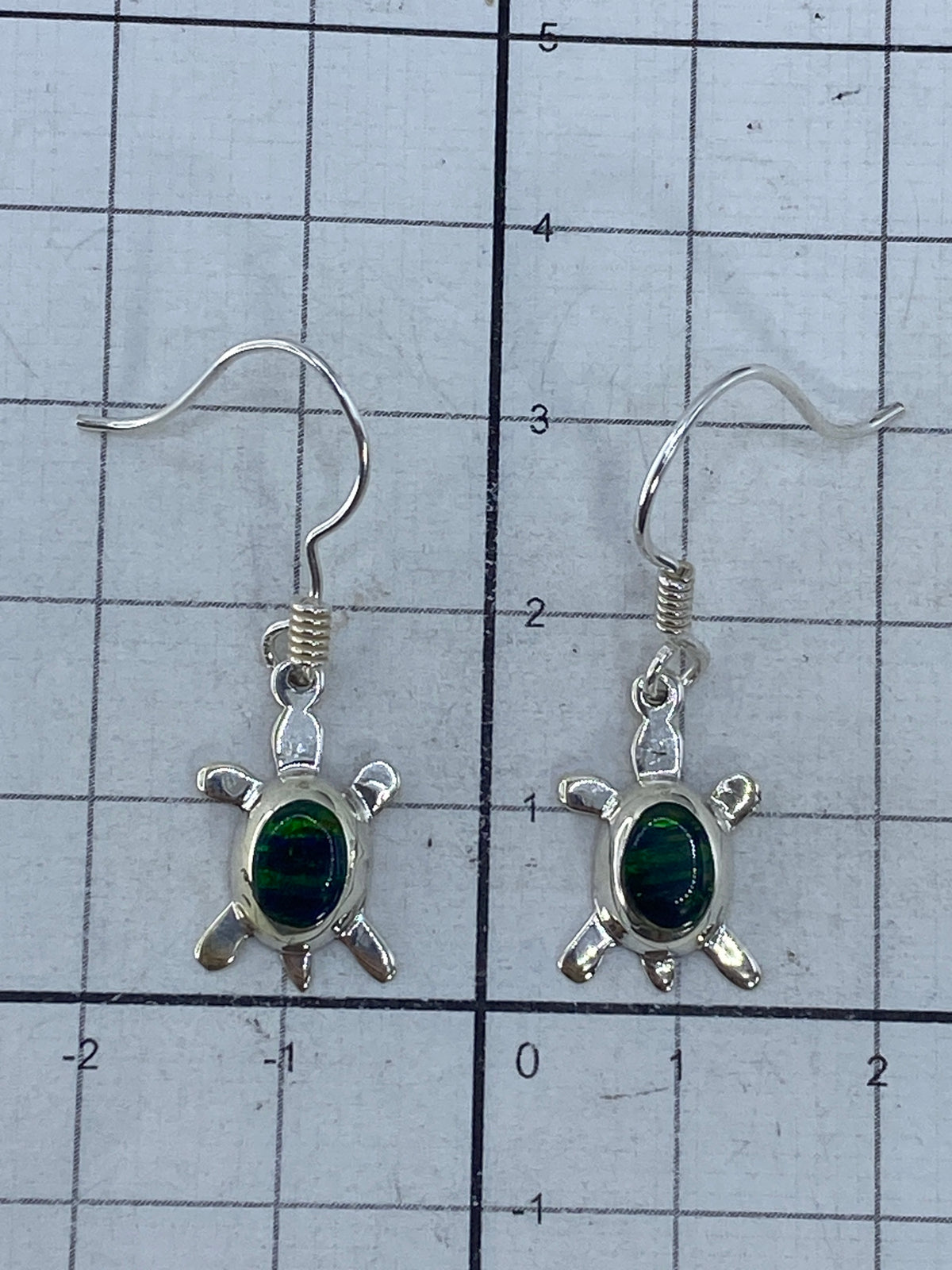 Aretes pequeños de tortuga con piedra verde junto a regla de centímetros, mostrando tamaño 3.3 cm