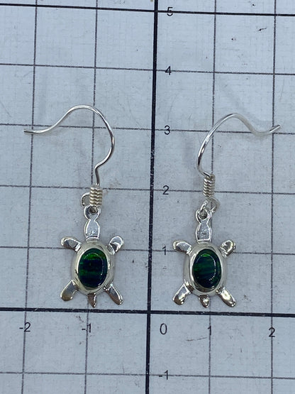 Aretes pequeños de tortuga con piedra verde junto a regla de centímetros, mostrando tamaño 3.3 cm