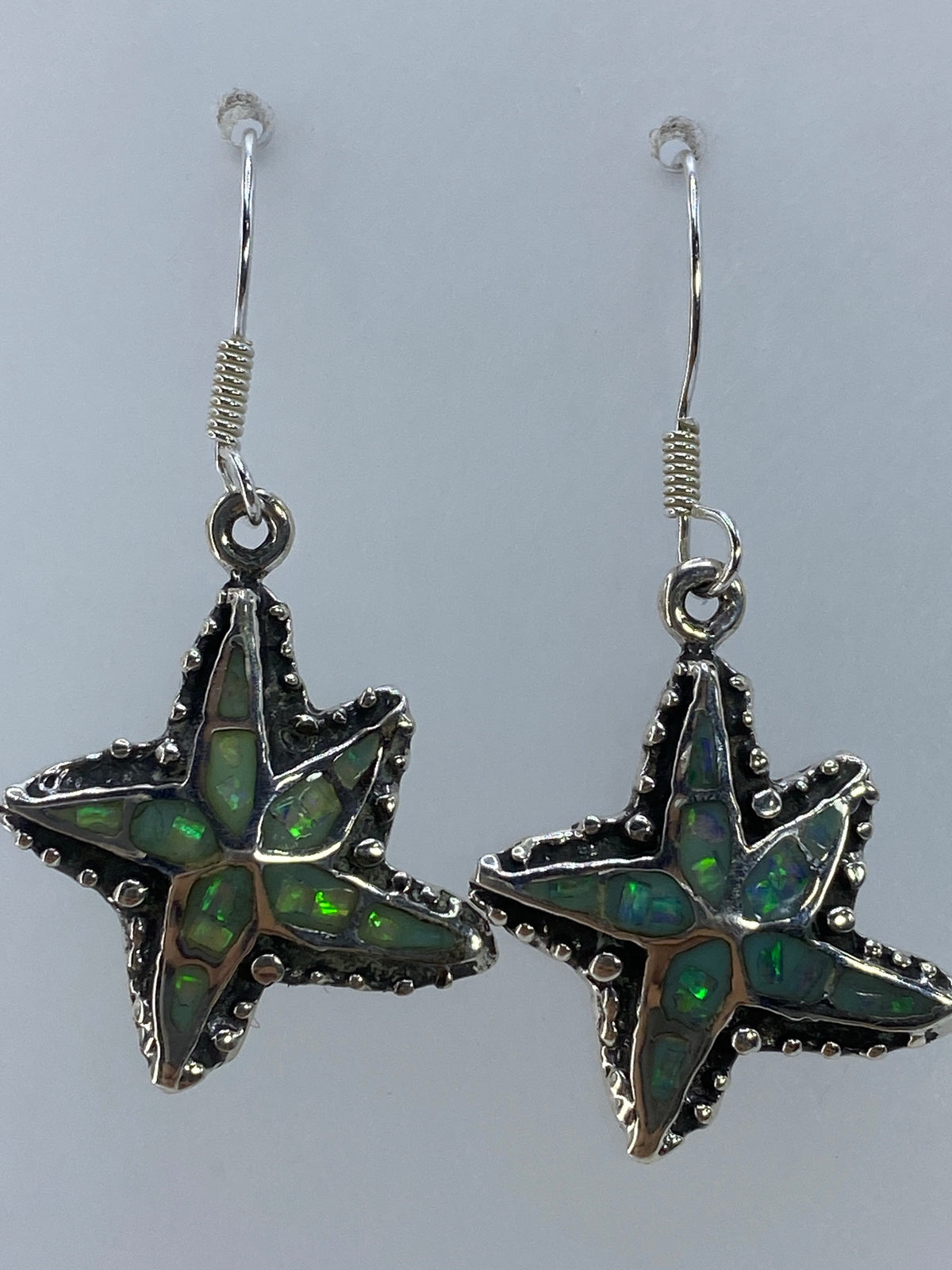 Par de aretes de plata con ópalo de fuego verde olivo, colgando sobre fondo blanco