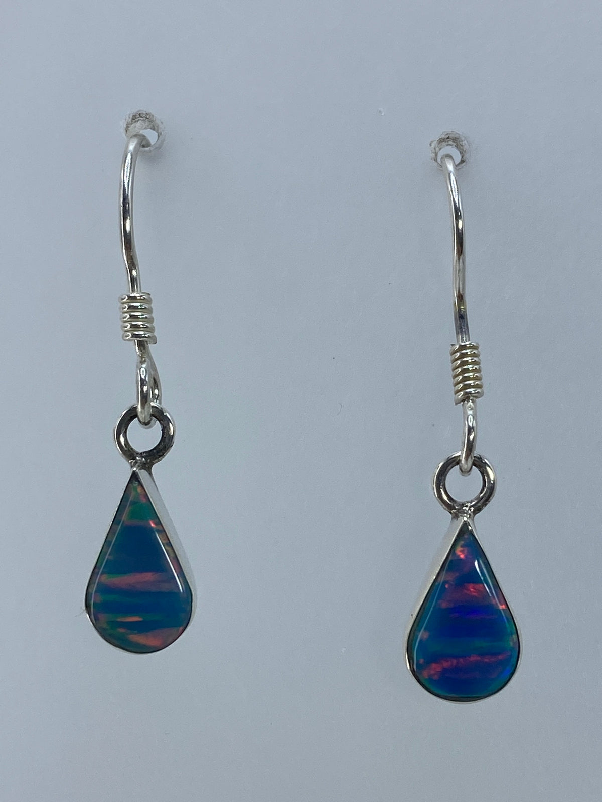 Par de aretes de plata con ópalo de fuego multicolor, mostrando el juego de colores naranja, azul y verde