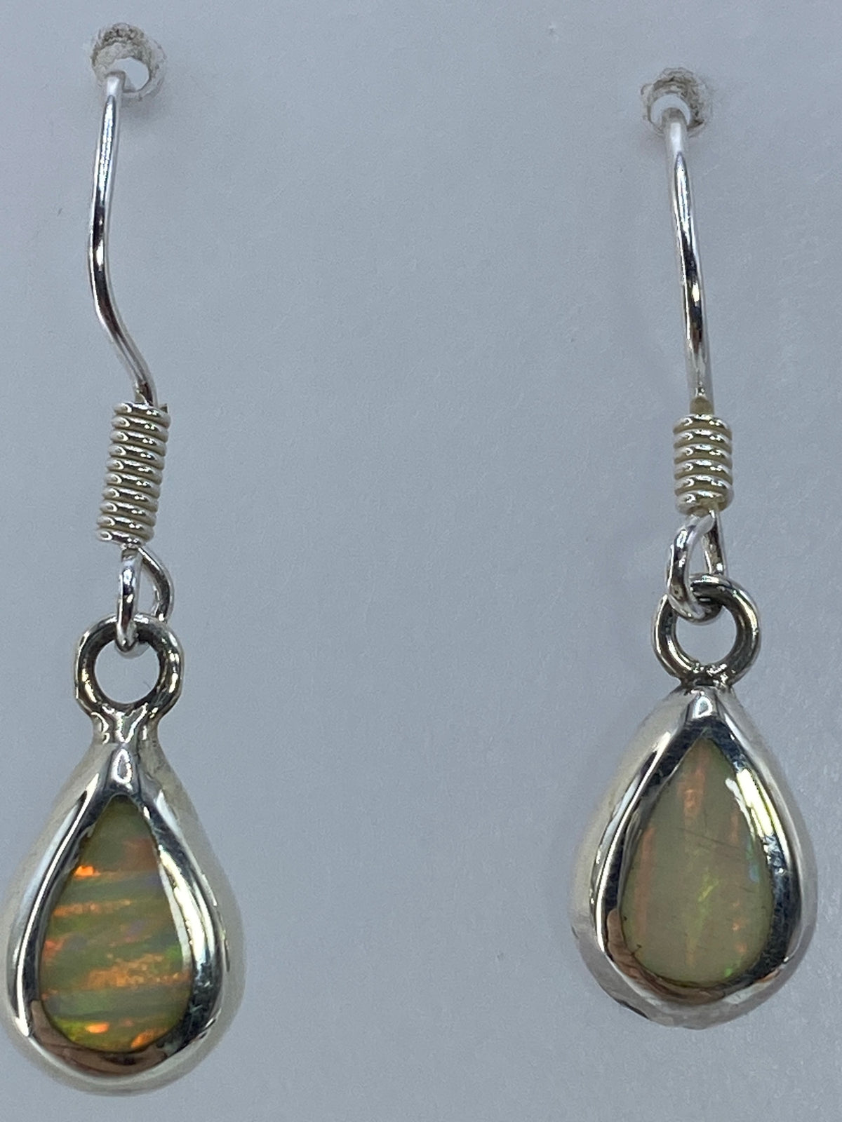 Aretes de plata 950 con ópalo de fuego en gancho, vistos desde arriba sobre fondo gris