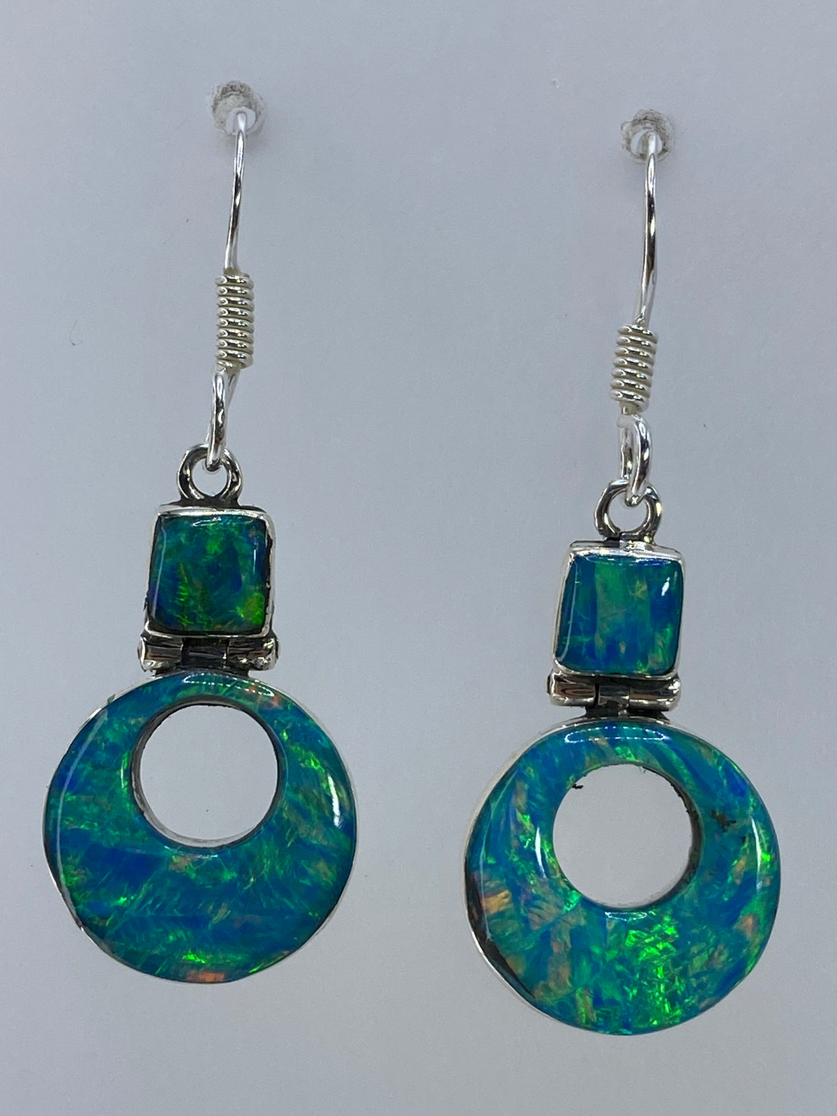 Par de aretes de plata con ópalo de fuego verde olivo colgando sobre fondo gris