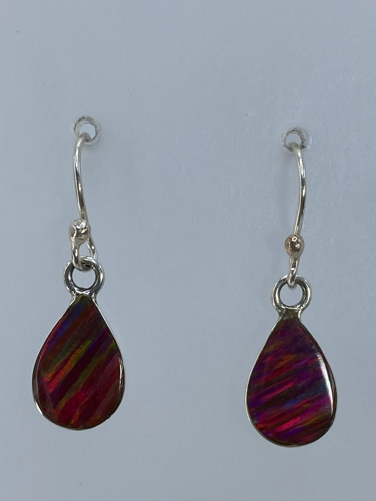 Aretes de plata con ópalo de fuego multicolor colgando, destellos rojos, naranjas y verdes