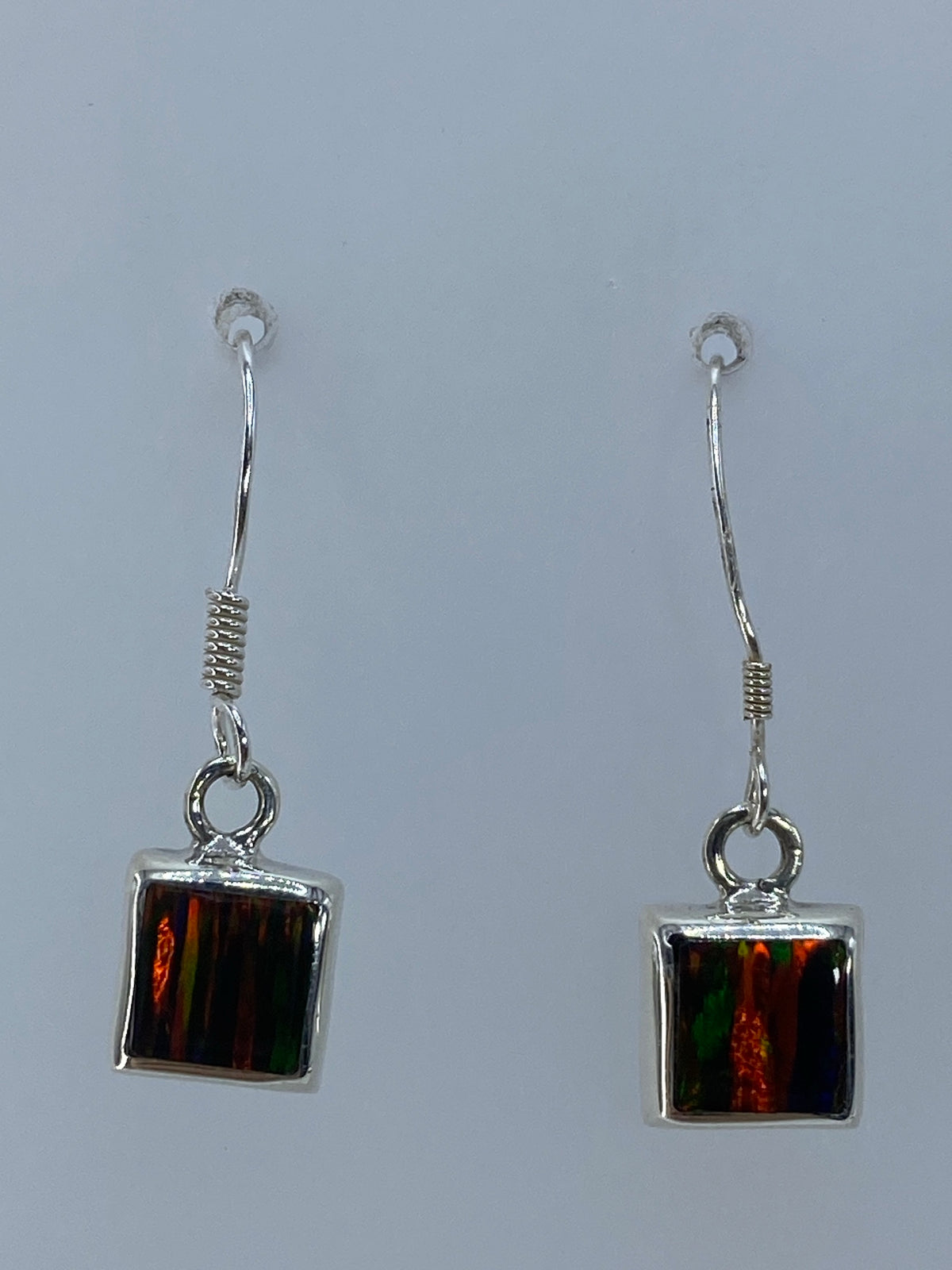 Aretes de plata con ópalo de fuego multicolor colgando de un par de orejas