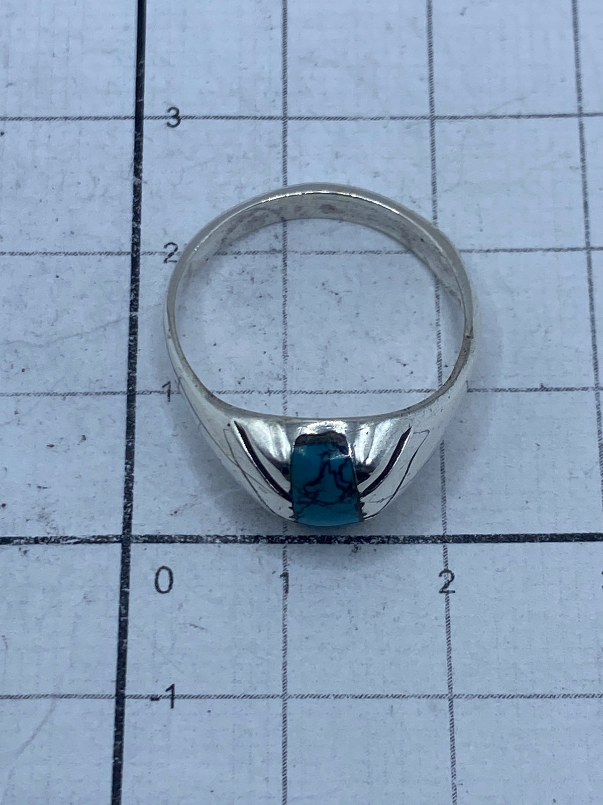 Anillo sobre fondo gris mostrando el acabado pulido de la plata y el azul profundo de la turquesa