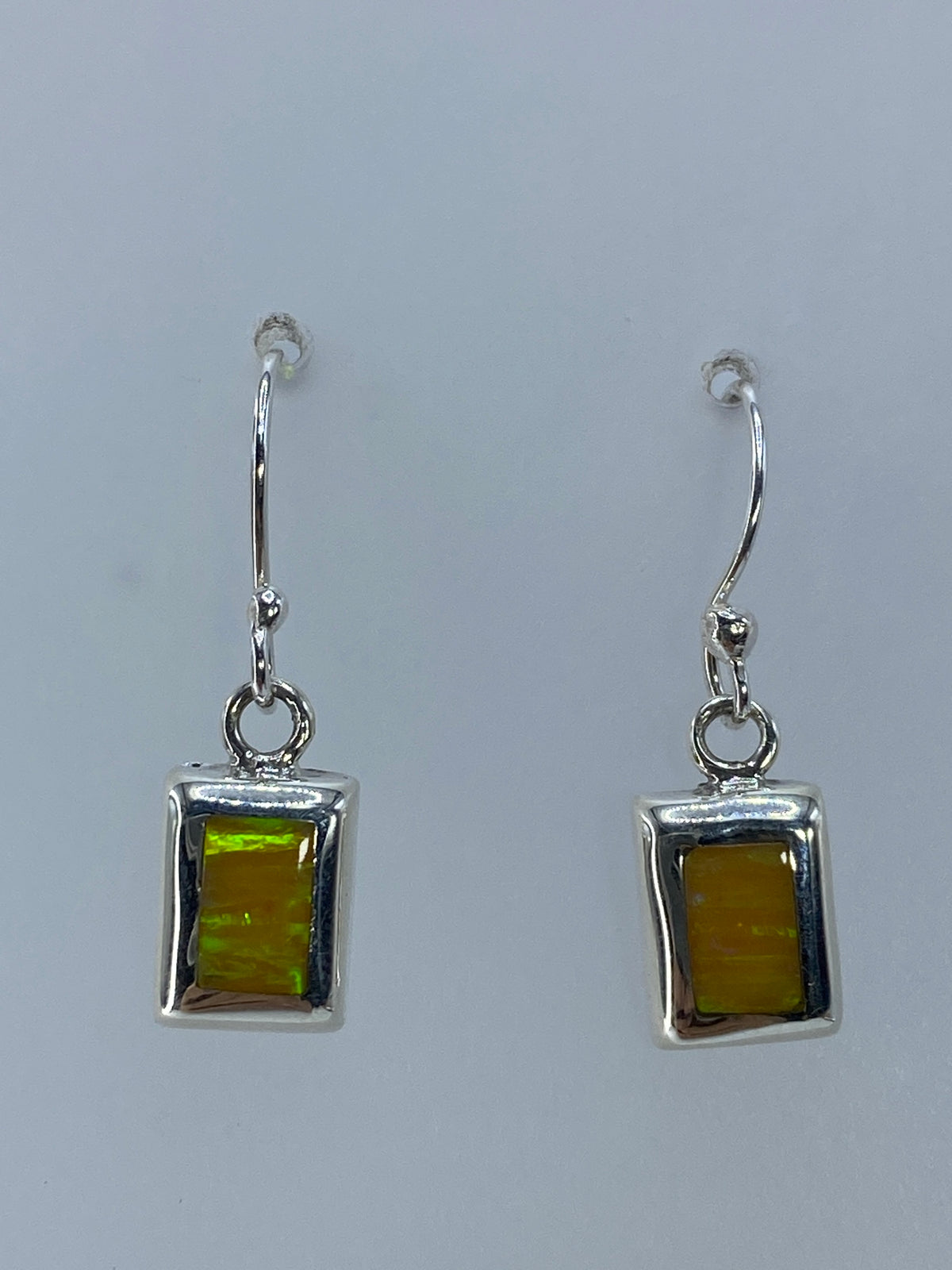 Vista frontal de los aretes con ópalo de fuego brillando en tonos amarillos y naranjas