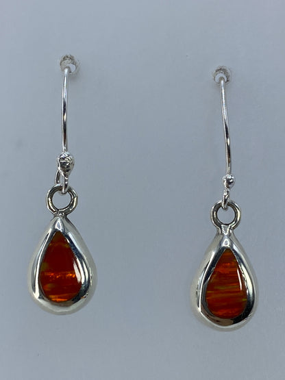 Par de aretes de plata con ópalo de fuego naranja engastado, colgando sobre fondo gris