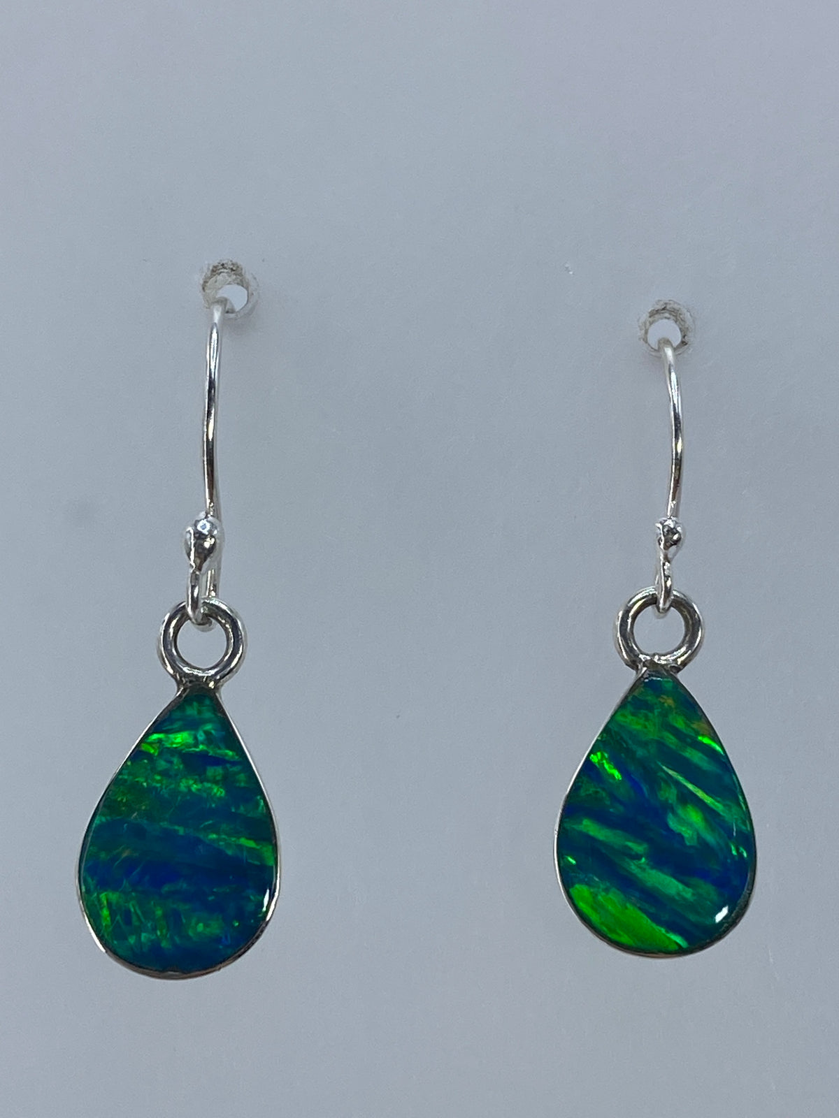 Aretes de plata con opalo de fuego verde limon, colgando sobre fondo gris