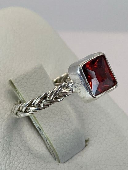 Anillo de plata trenzada con circonia roja brillante en la mano