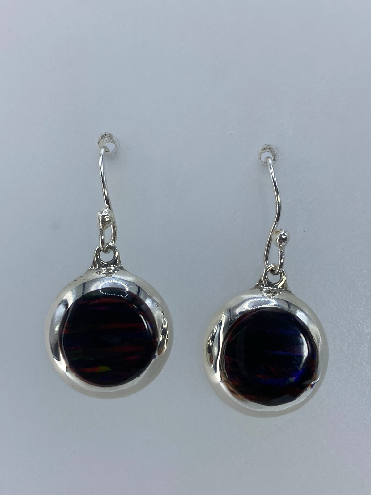 Arete individual de plata con ópalo de fuego multicolor en la mano