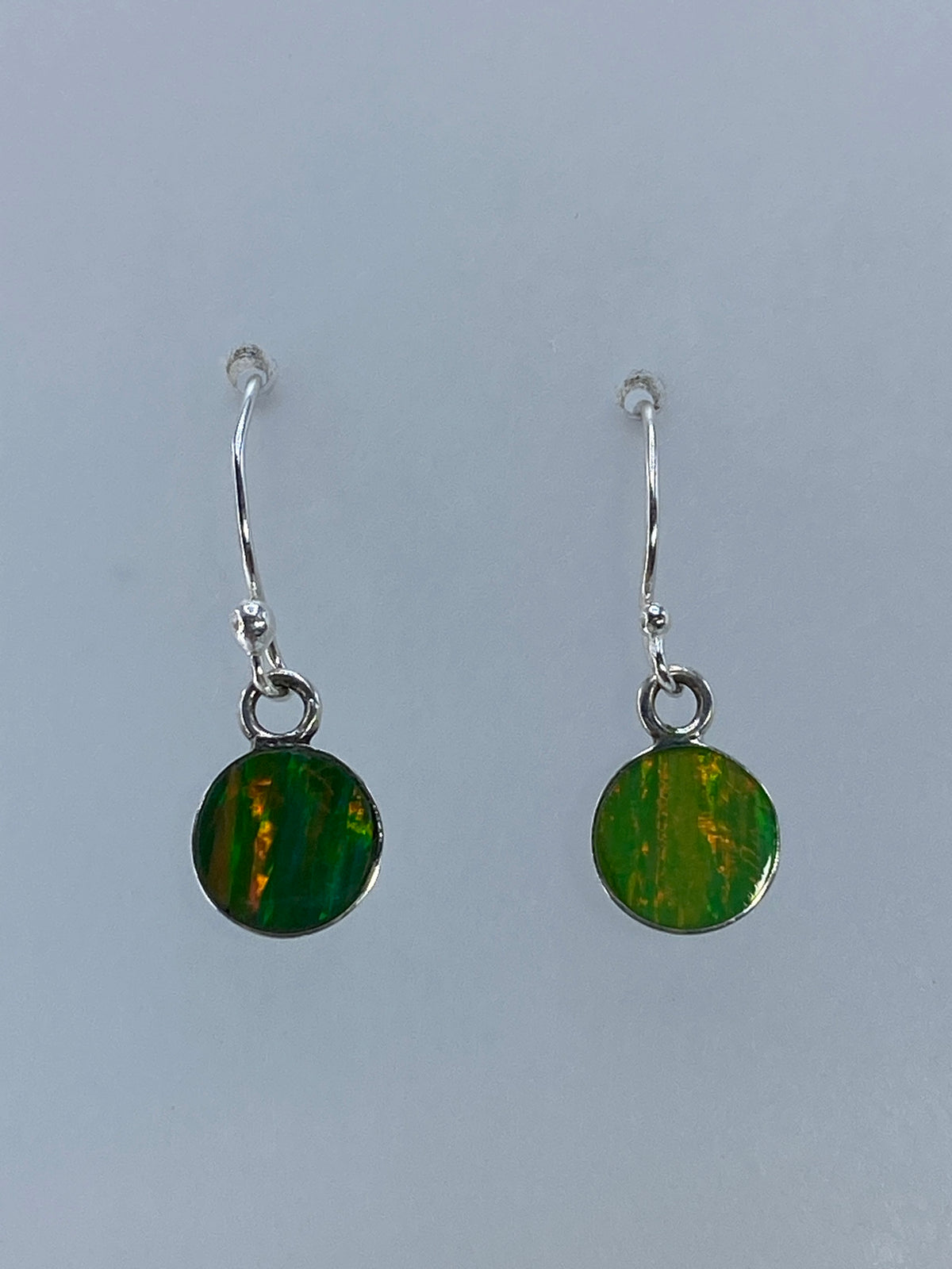Aretes de ópalo de Fuego colgando, mostrando los destellos naturales de la piedra