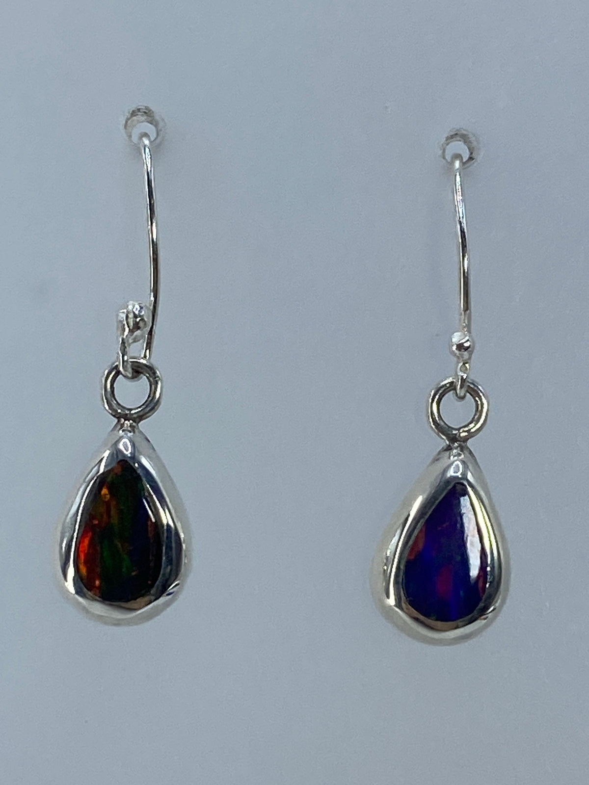 Par de aretes de plata con ópalo de fuego multicolor mostrando destellos rojo, naranja y azul