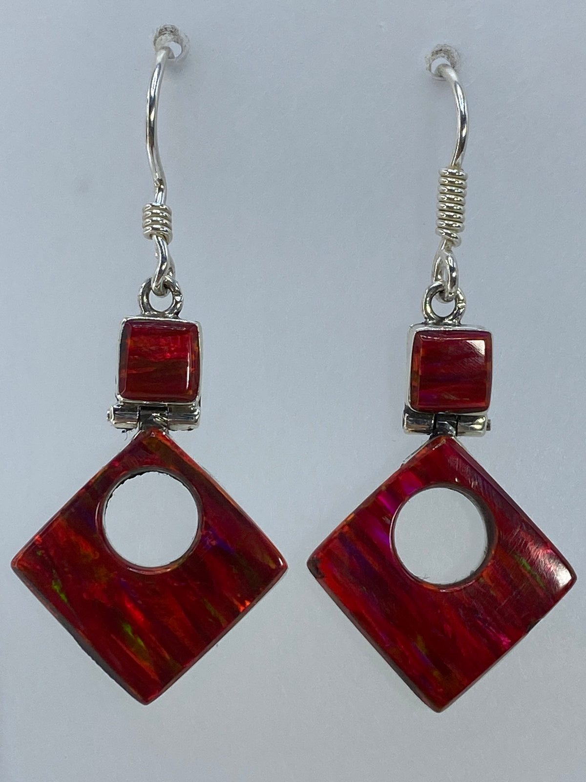 Aretes de plata con ópalo de fuego rojo, forma geométrica cuadrada, colgando sobre fondo blanco