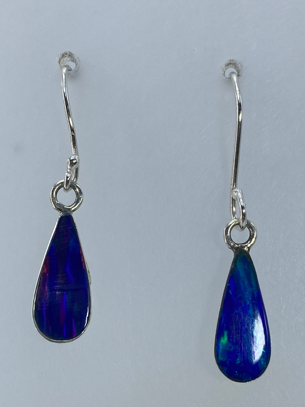 Aretes de plata con ópalo de fuego multicolor colgando del gancho, vista frontal
