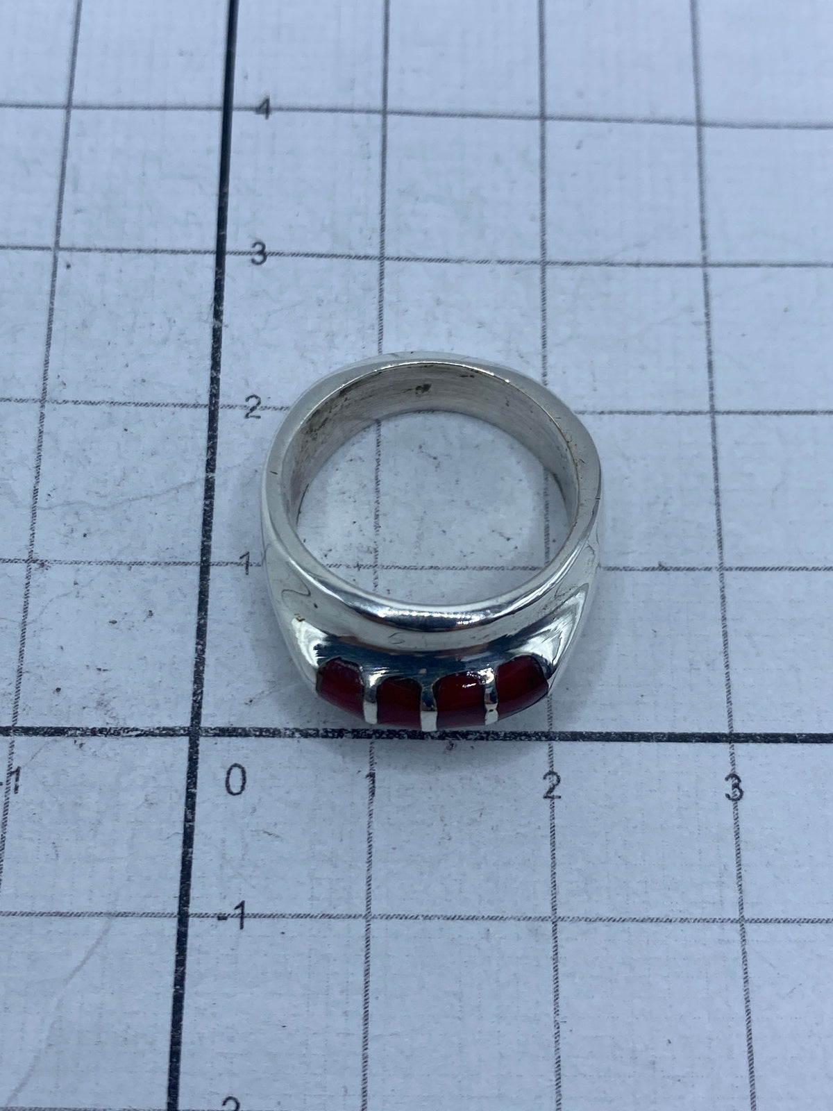 Anillo de plata con coral rojo puesto en el dedo, mostrando el brillo y el color cálido