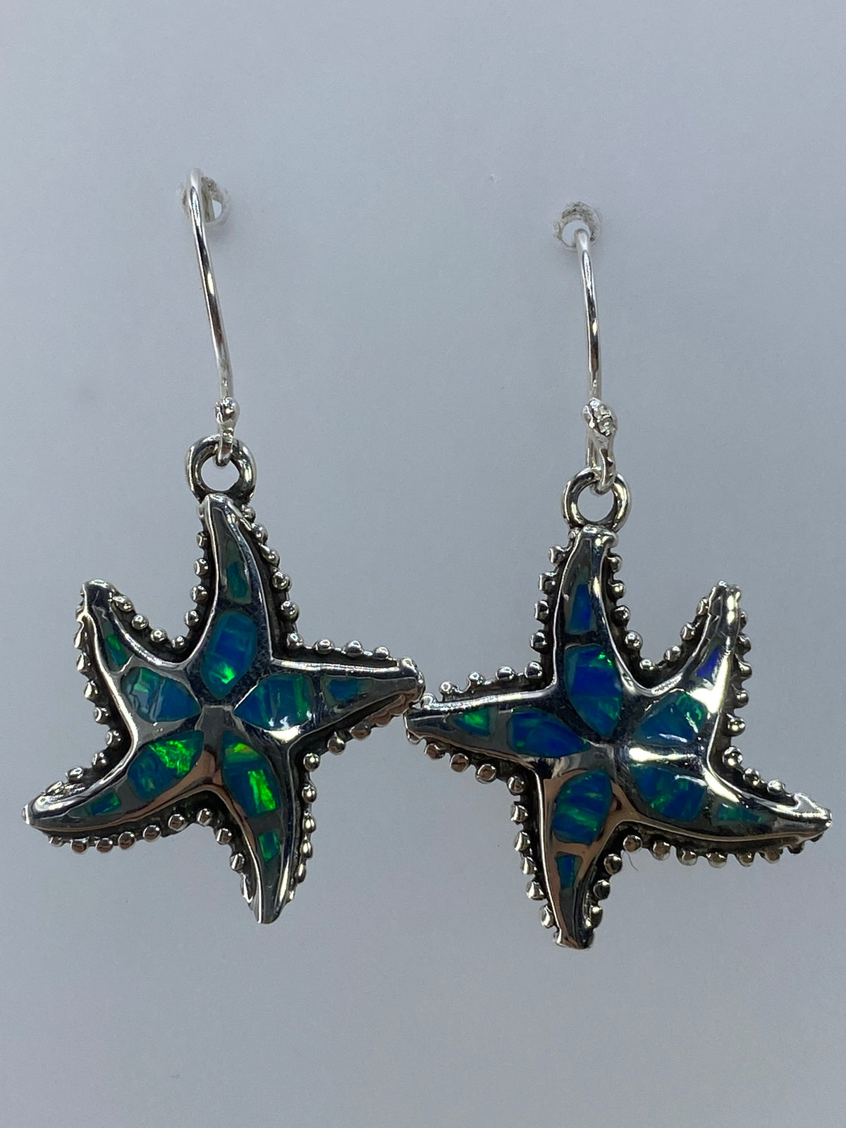 Aretes en par de plata con ópalo de fuego verde olivo, colgando sobre fondo gris neutro